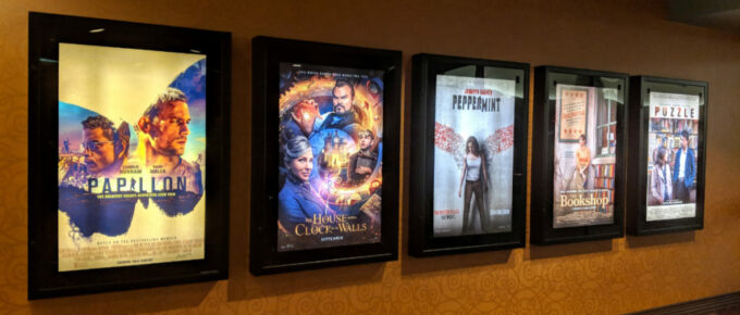 Row of movie posters including Papillon, the House with a Clock in it's Wall, Peppermint, The Bookshop, and Puzzle on a movie theatre wall